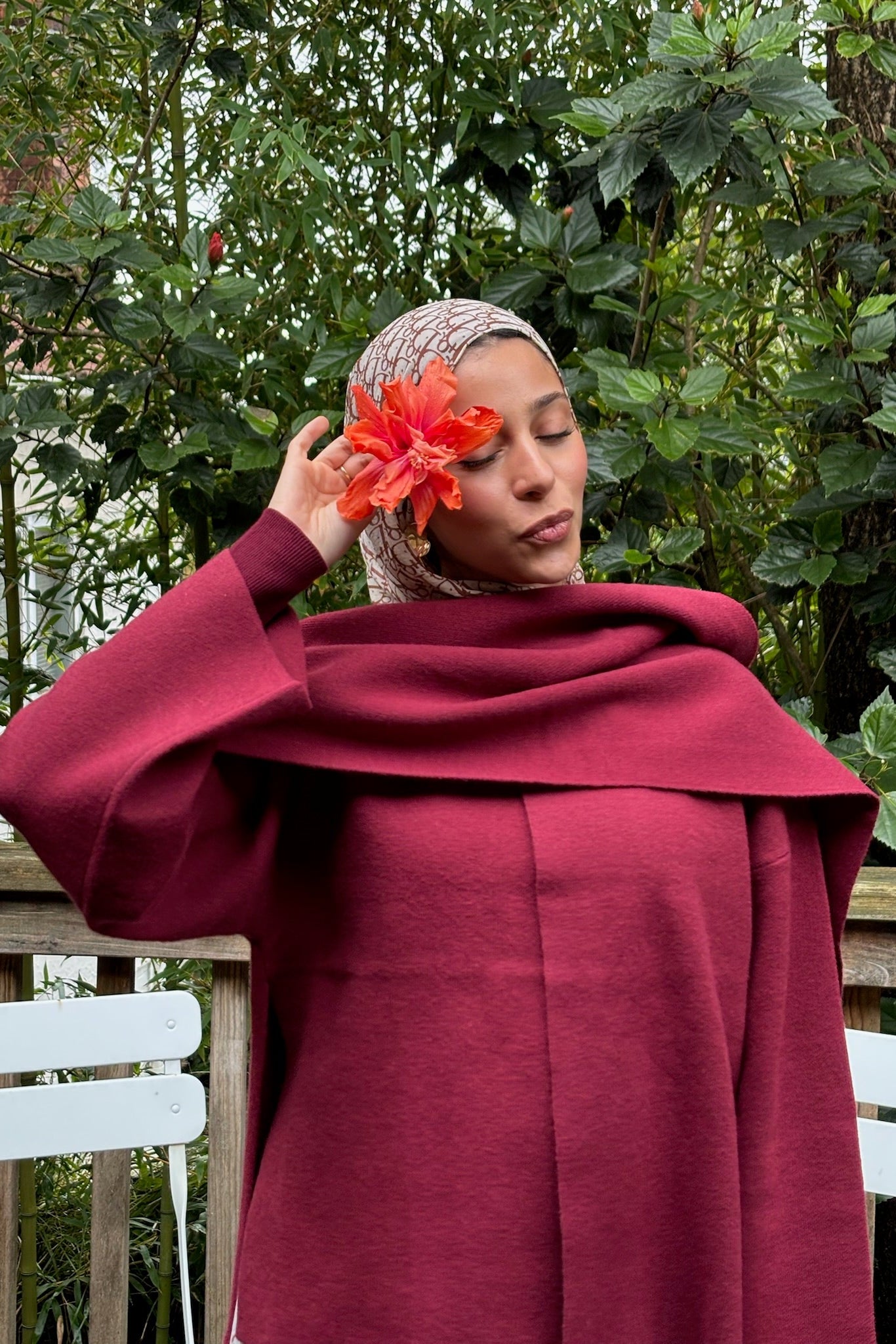 Woman in a burgundy outfit holding an orange flower outdoors