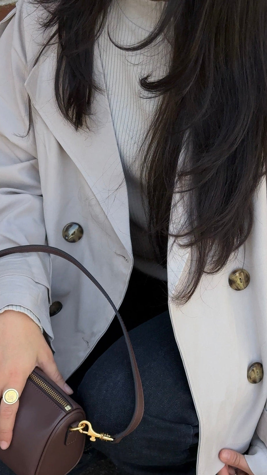 Person wearing a light-colored coat holding a brown handbag.