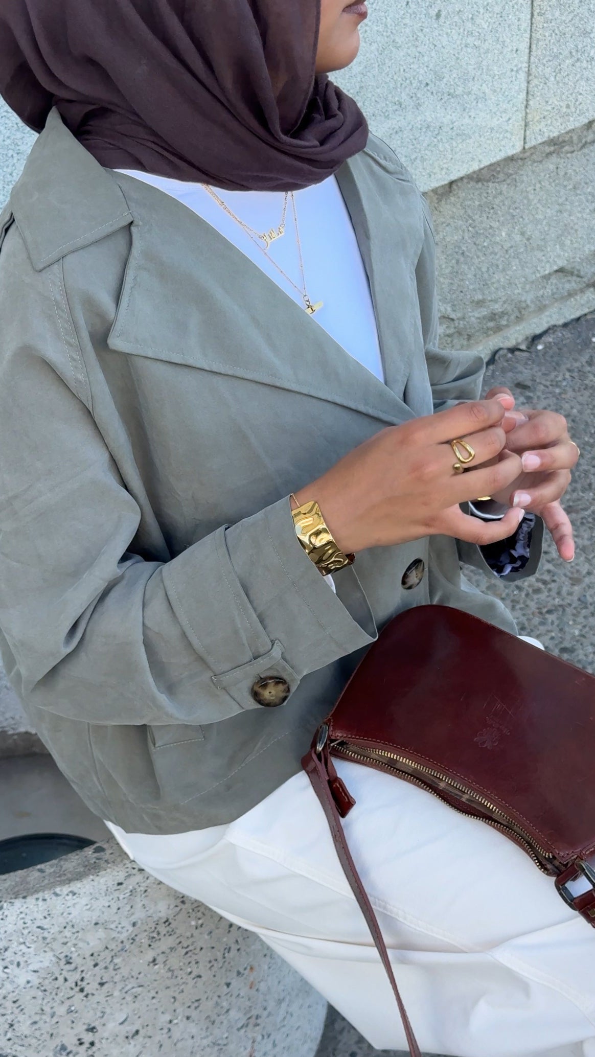 Person wearing a gray blazer and white pants, holding a brown handbag.